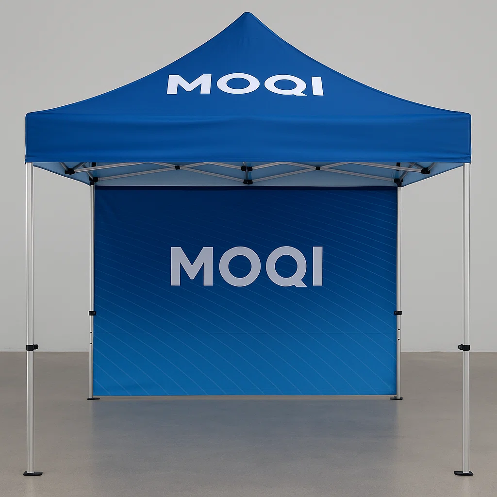 Ein vollständig aufgebautes Zelt mit dem MOQI-Logo, das in einer Messehalle ausgestellt wird. Das Zelt verfügt über ein kräftiges blaues Vordach mit dem MOQI-Logo auf dem Volant und der Rückwand.